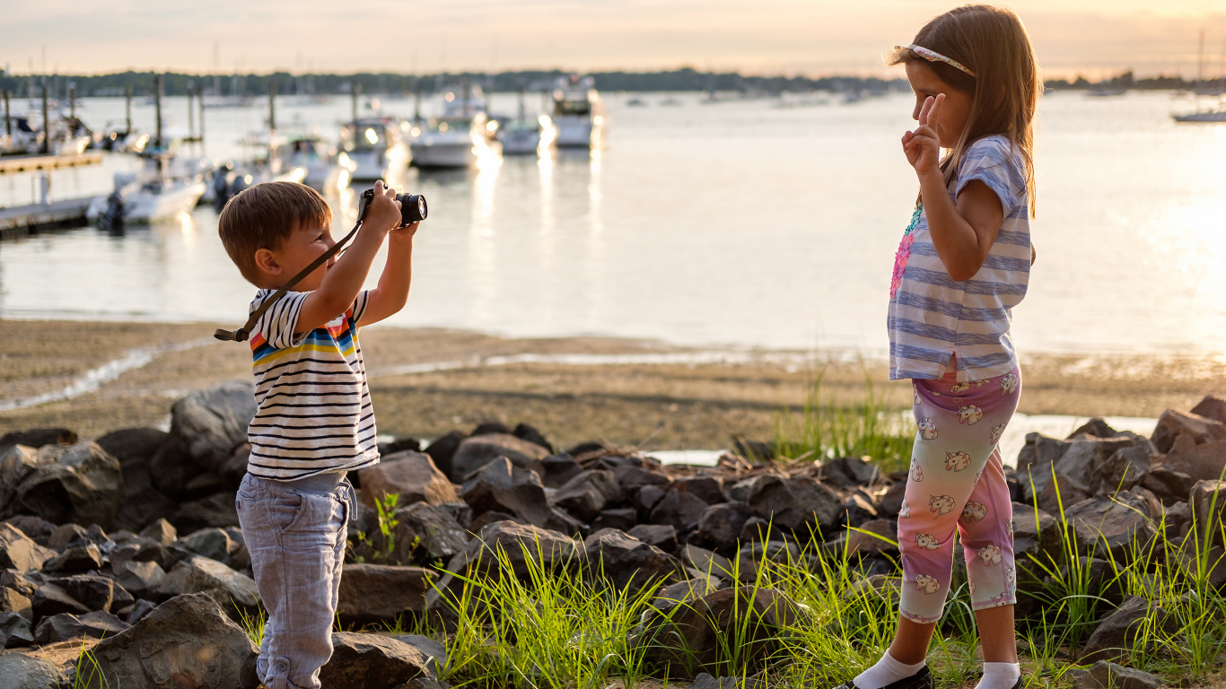 Маленький мальчик фотографирует девочку на берегу