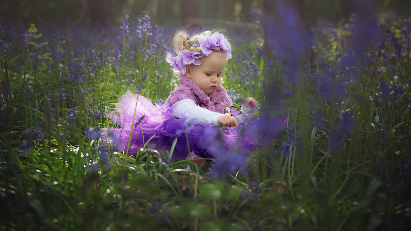 Маленькая девочка в красивом платье сидит в цветах с бабочкой на руке