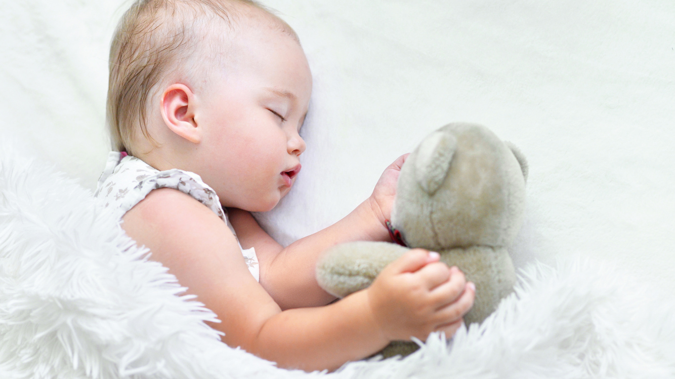 Маленькая девочка спит с мягкой игрушкой под белым одеялом