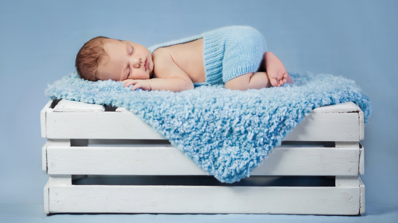 Маленький грудной ребенок спит на синем покрывале на деревянном ящике