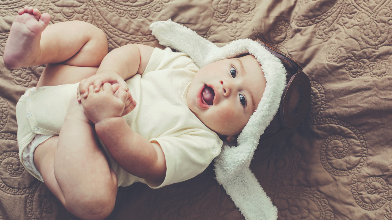 Маленький грудной ребенок лежит в шапке летчика