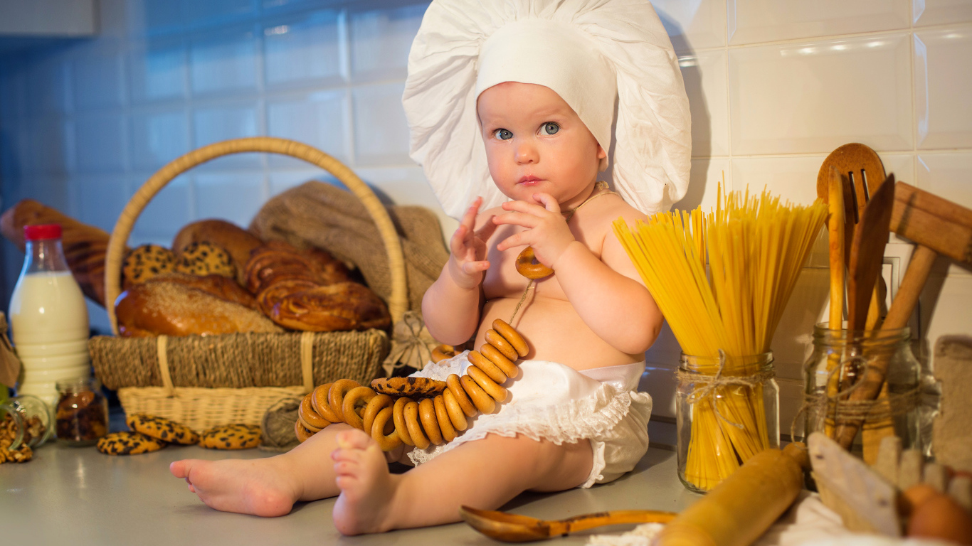 Маленький ребенок в шапке повара сидит на столе с выпечкой