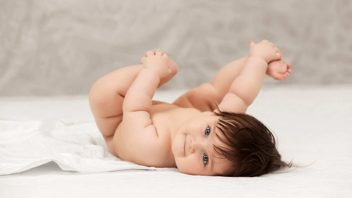 Забавный младенец держится руками за ноги 
