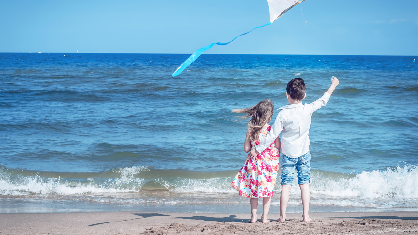 Маленькие мальчик и девочка запускаю воздушного змея на пляже