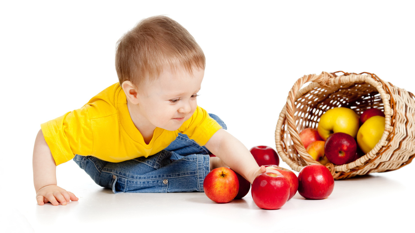 Маленький мальчик с корзиной спелых яблок на белом фоне
