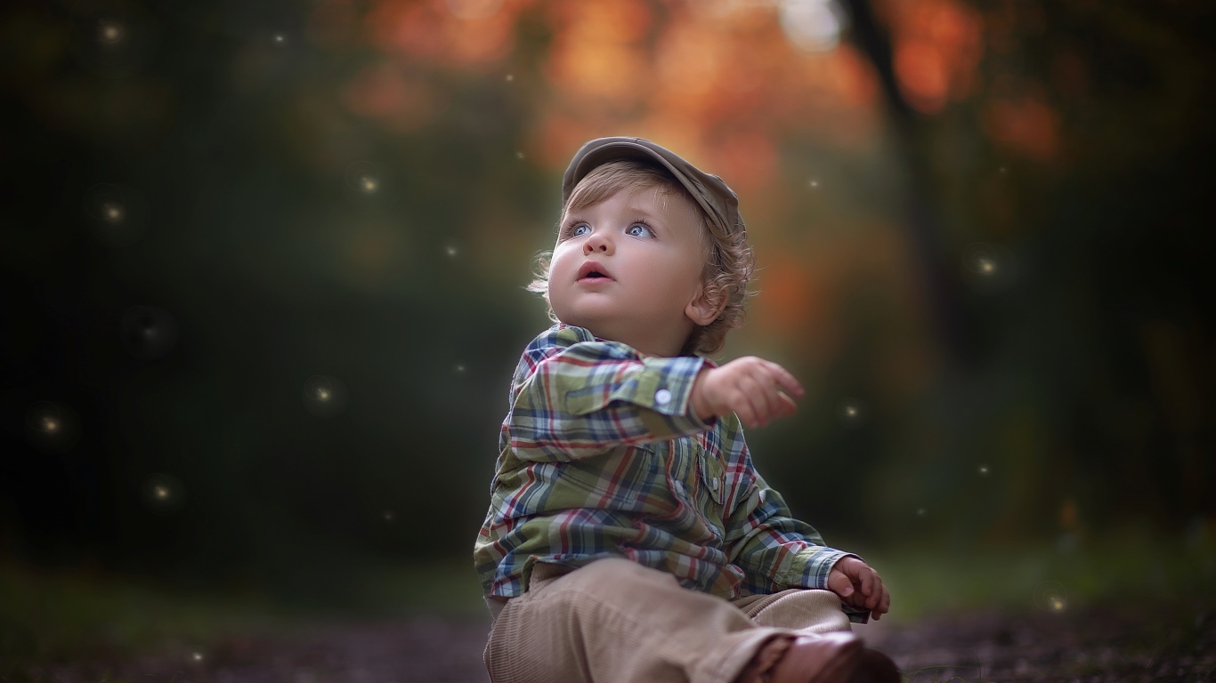 Маленький милый мальчик сидит в кепке на дороге