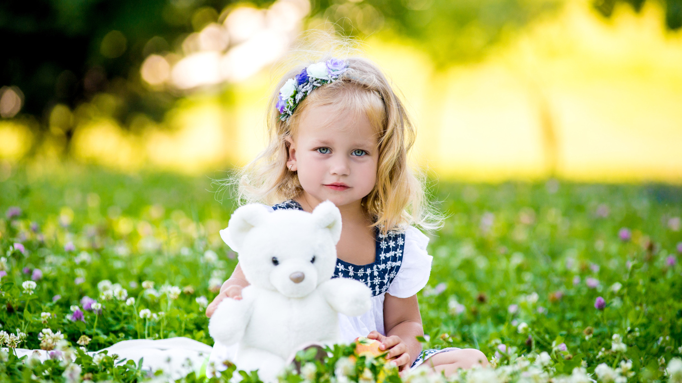 Маленькая милая девочка с игрушкой сидит на зеленой траве с цветами