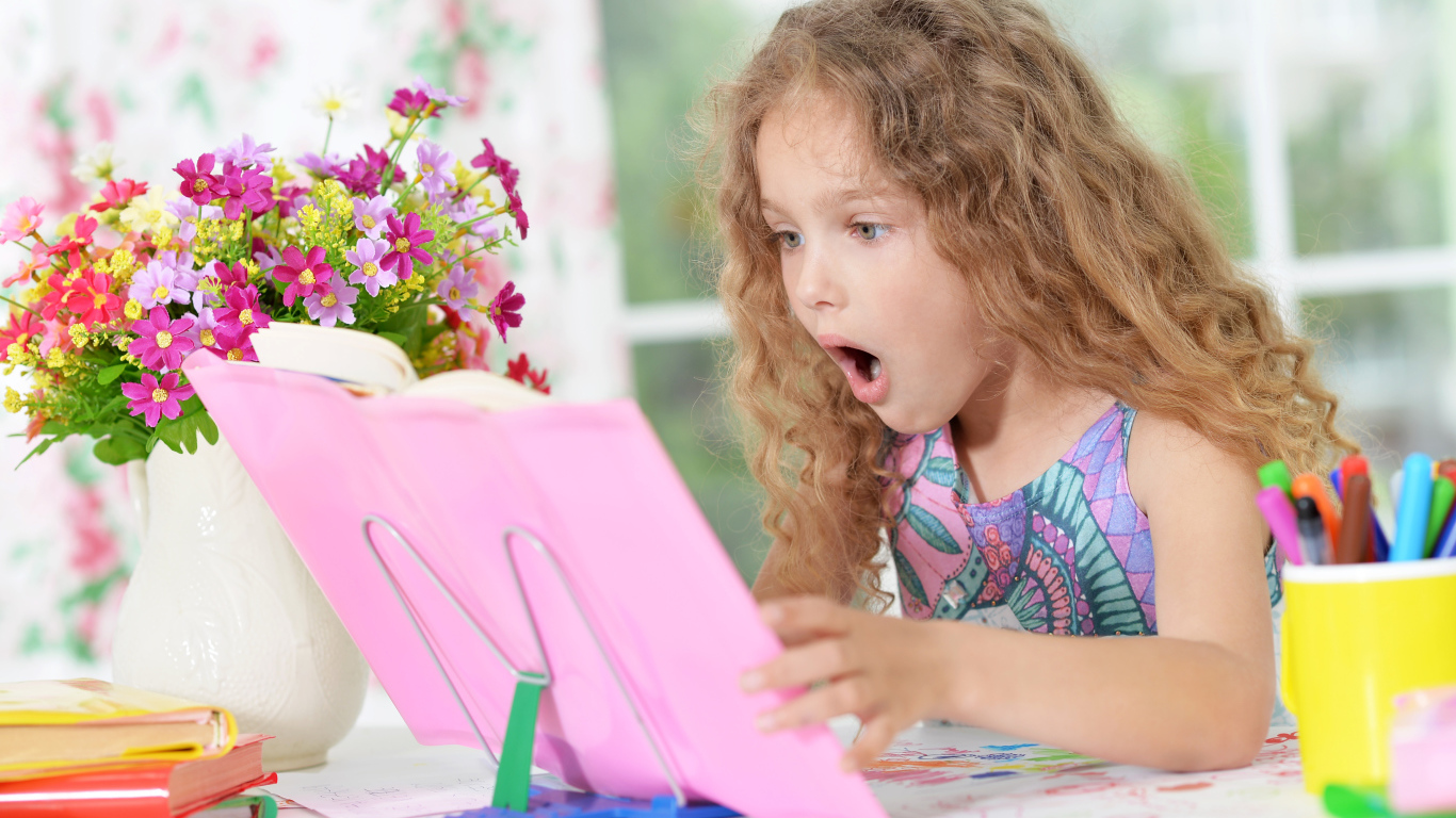 Маленькая русоволосая девочка удивленно смотрит в книгу