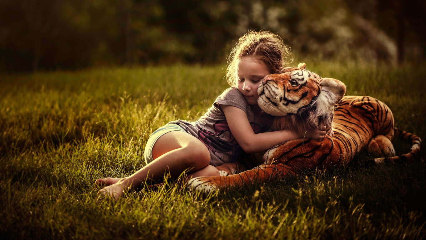 Маленькая девочка обнимает игрушечного тигра на зеленой траве