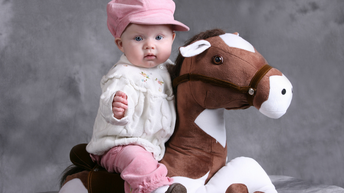 Маленькая девочка в розовой кепке сидит на игрушечной лошади