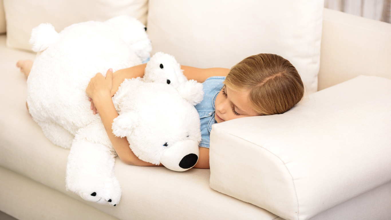 Маленькая девочка спит с белым плюшевым мишкой на диване