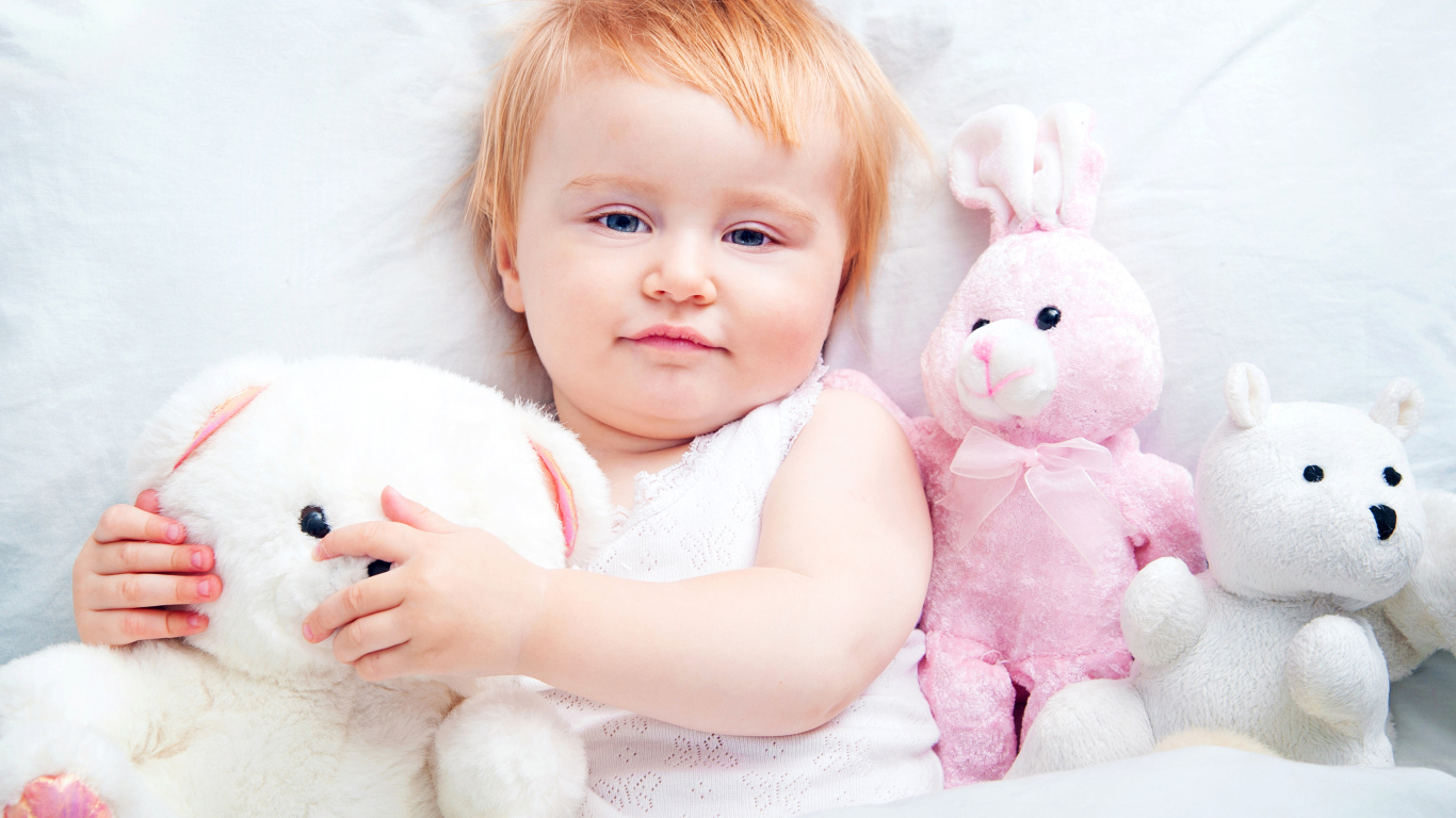 Маленькая девочка лежит в кровати с плюшевыми игрушками