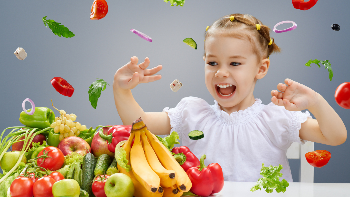 Маленькая девочка играет с овощами и фруктами на кухне