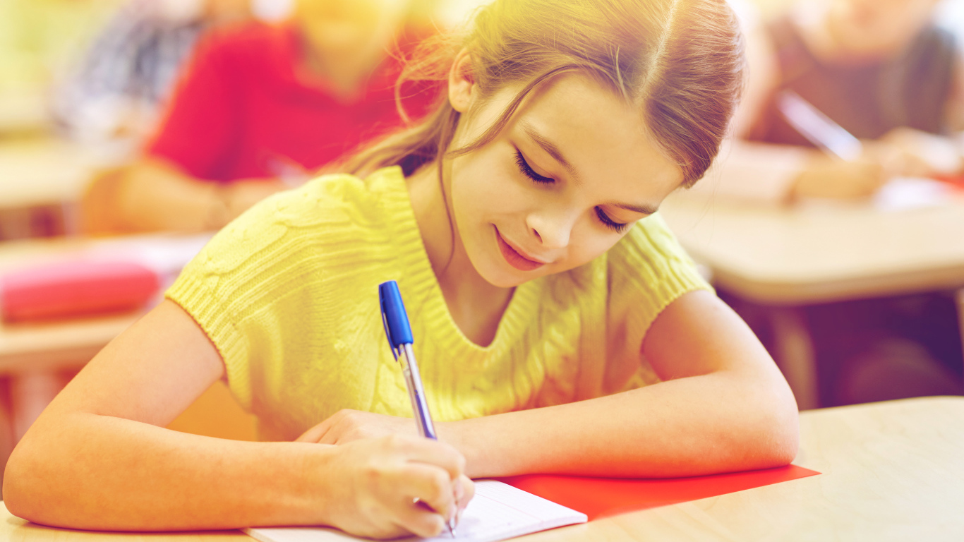 Маленькая девочка школьница пишет ручкой в тетради