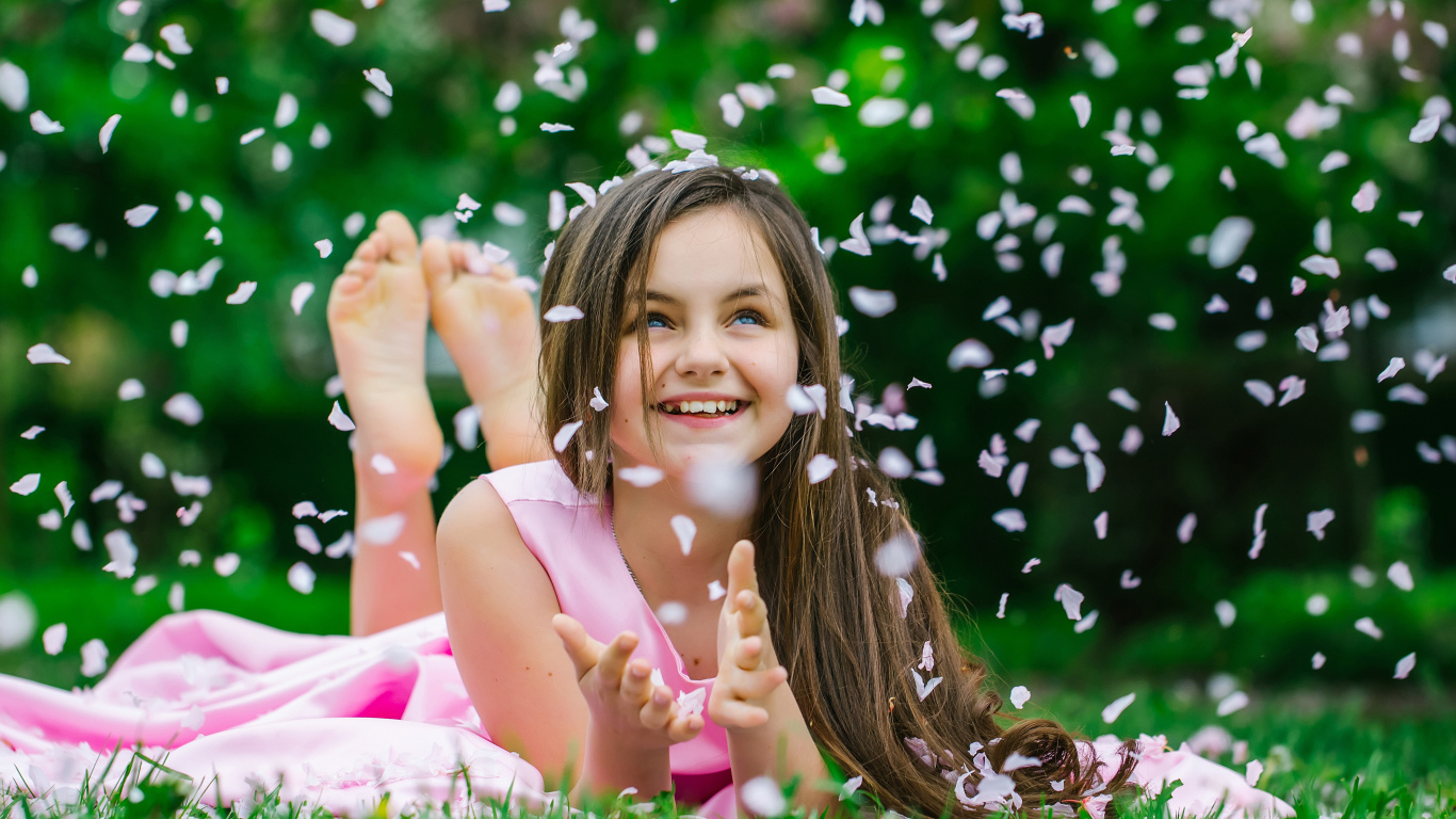 Маленькая улыбающаяся девочка шатенка ловит лепестки