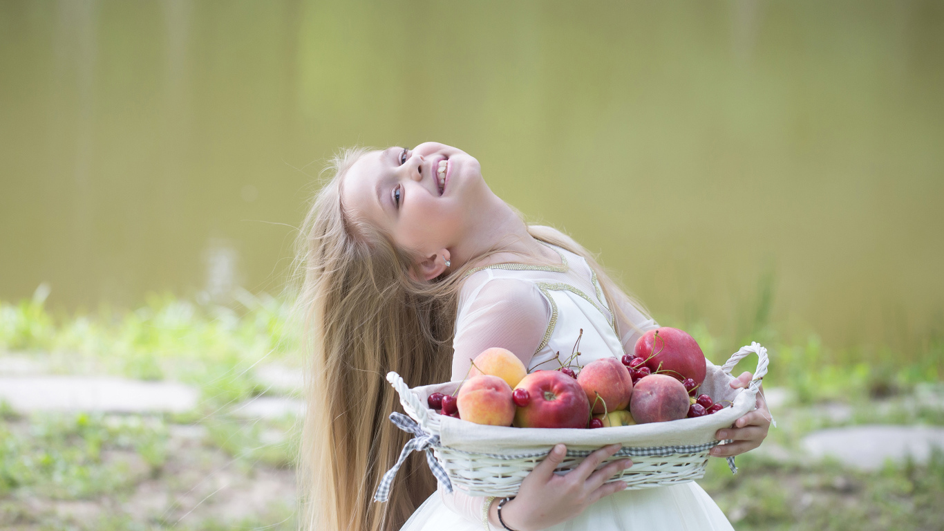 Маленькая улыбающаяся девочка в белом платье с корзиной фруктов