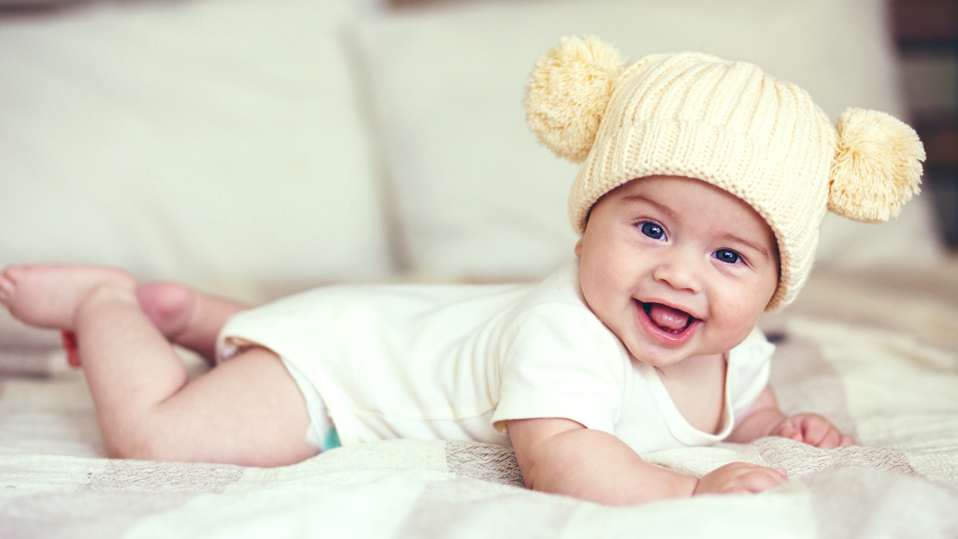 Улыбающийся грудной ребенок в забавной вязаной шапке