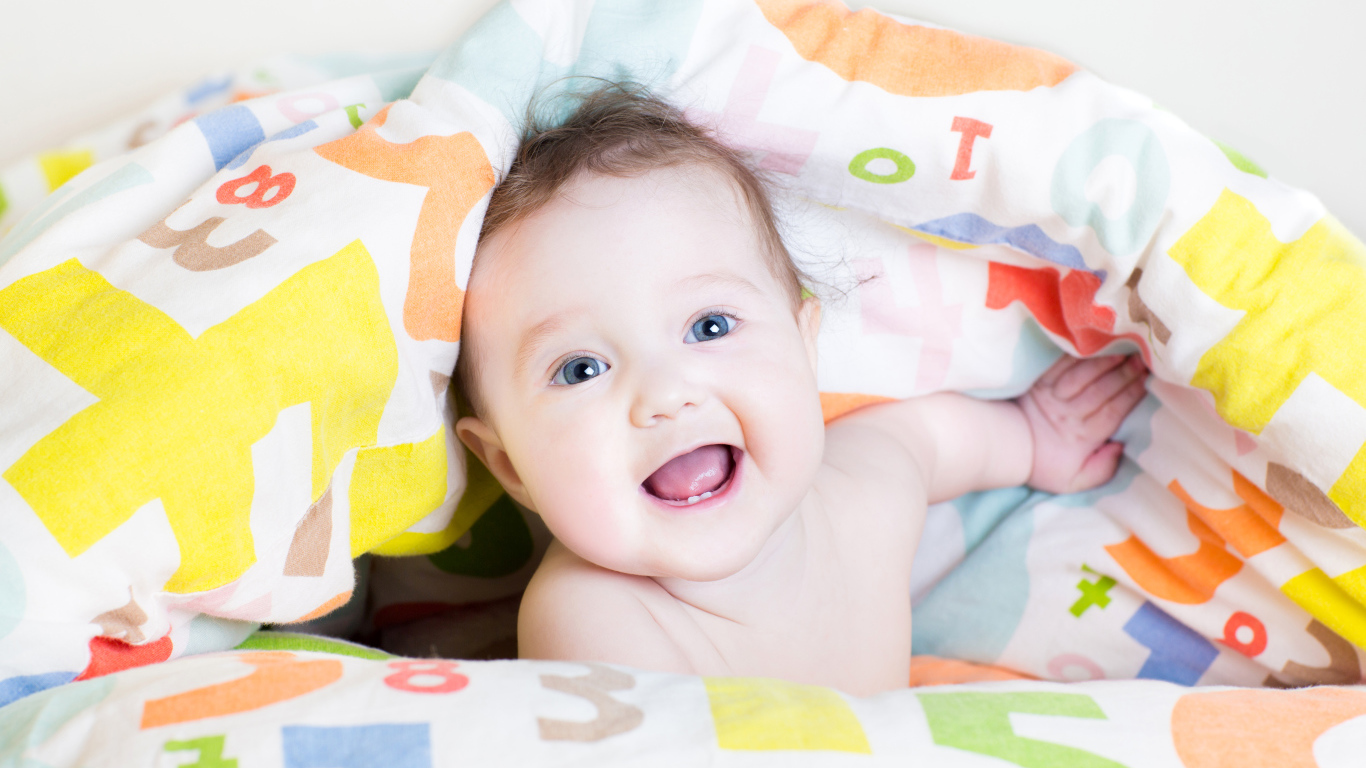 Улыбающийся голубоглазый ребенок под разноцветным покрывалом