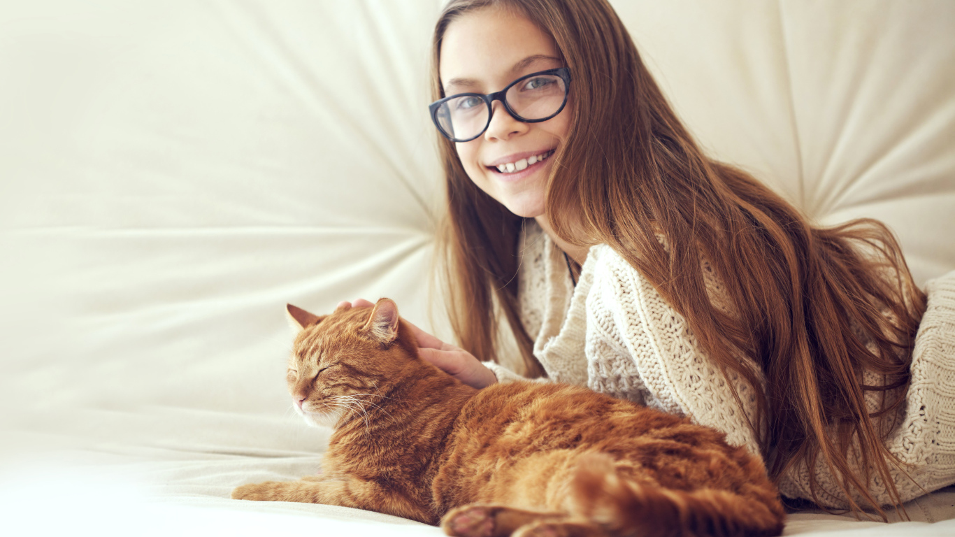 Улыбающаяся девочка шатенка в очках гладит рыжего кота