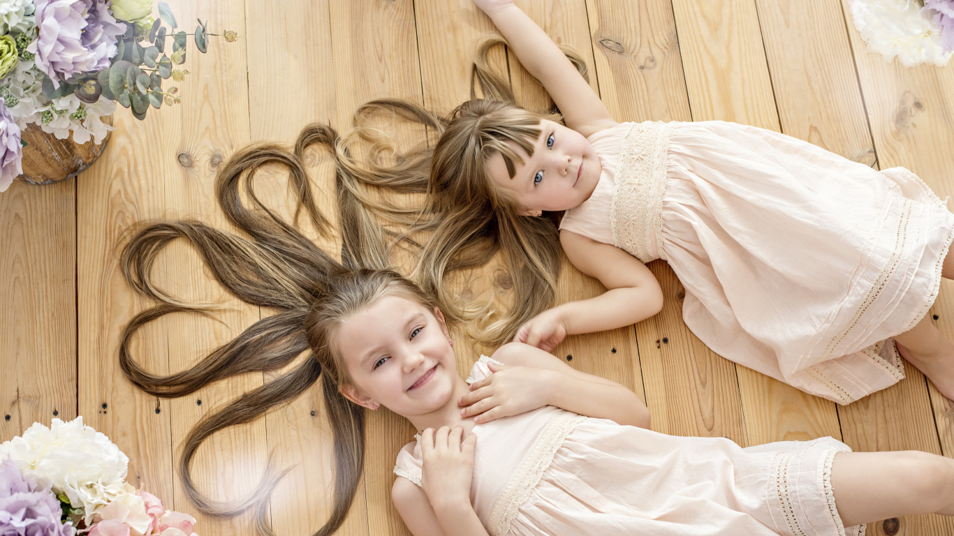 Две маленькие девочки с длинными волосами лежат на полу