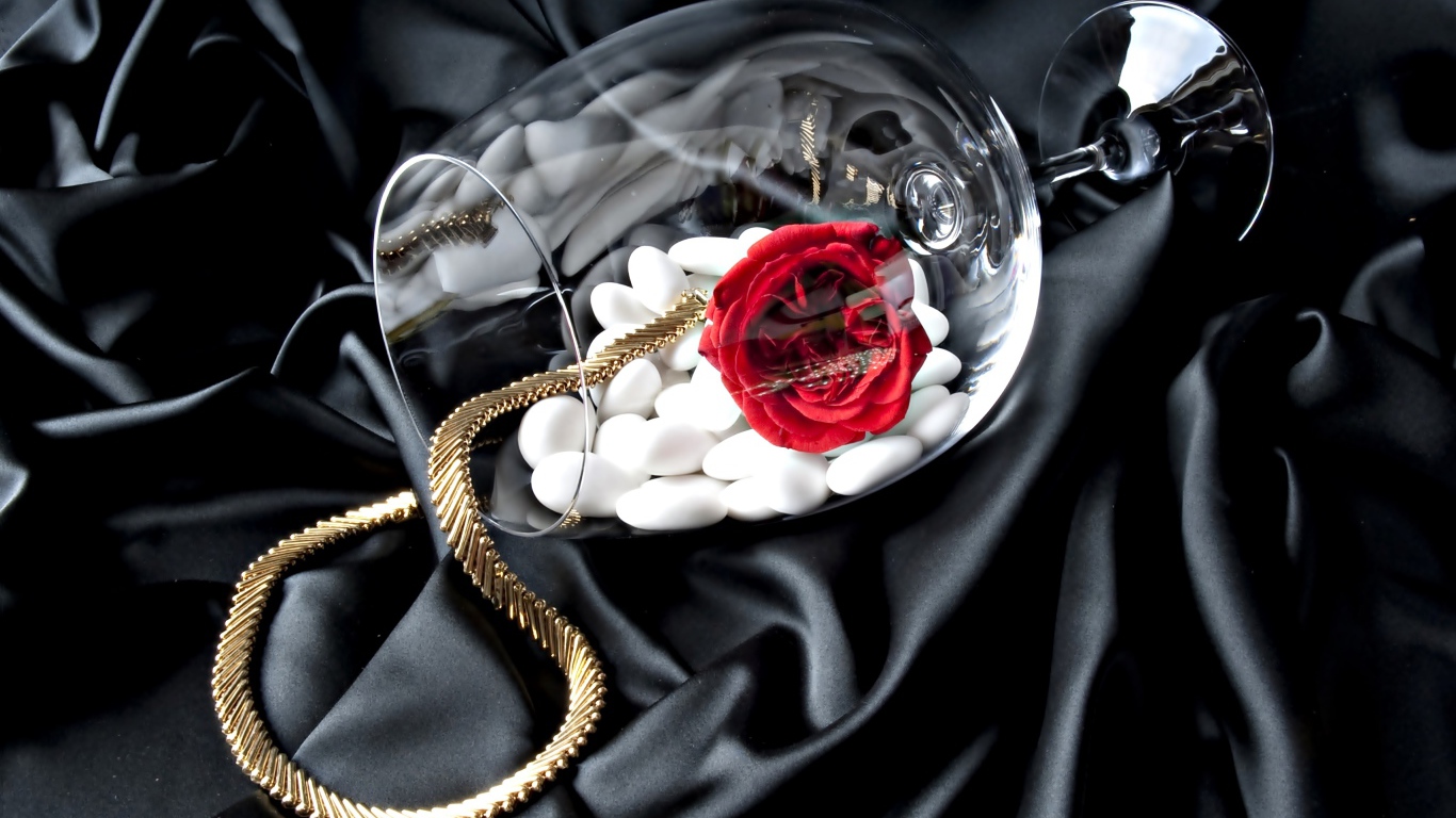 Бокал с золотой цепочкой, красной розой и белыми камнями на черном покрывале