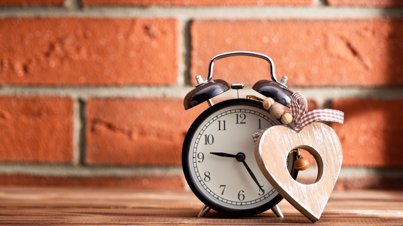 Будильник с деревянным сердцем стоит на фоне стены