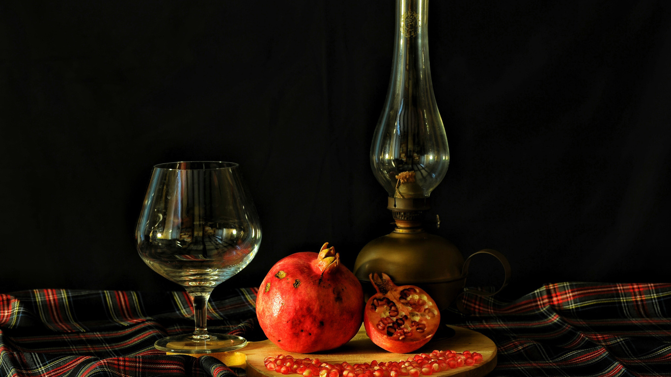 Керосиновая лампа, гранат и бокал на черном фоне