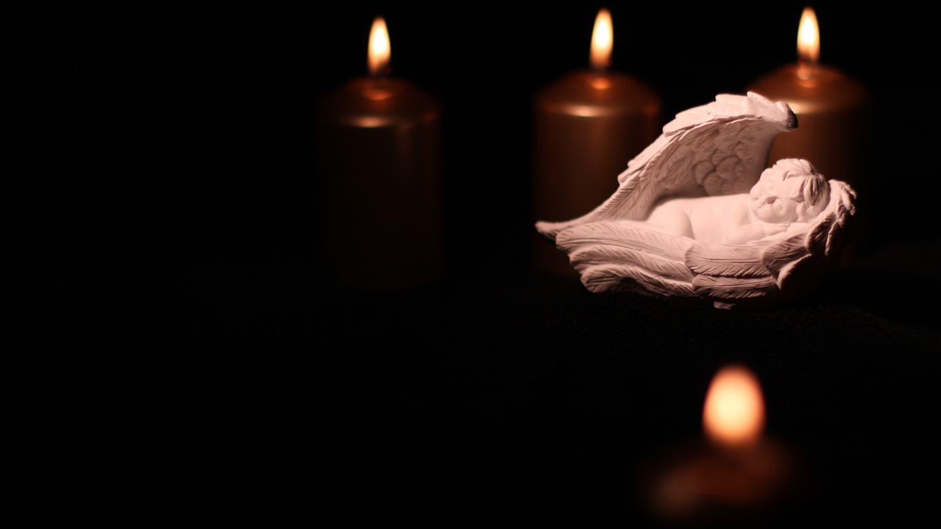 Фигурка ангела освещен горящими свечами на черном фоне