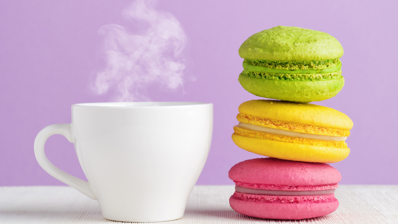 Разноцветный десерт макарун с чашкой горячего кофе на столе