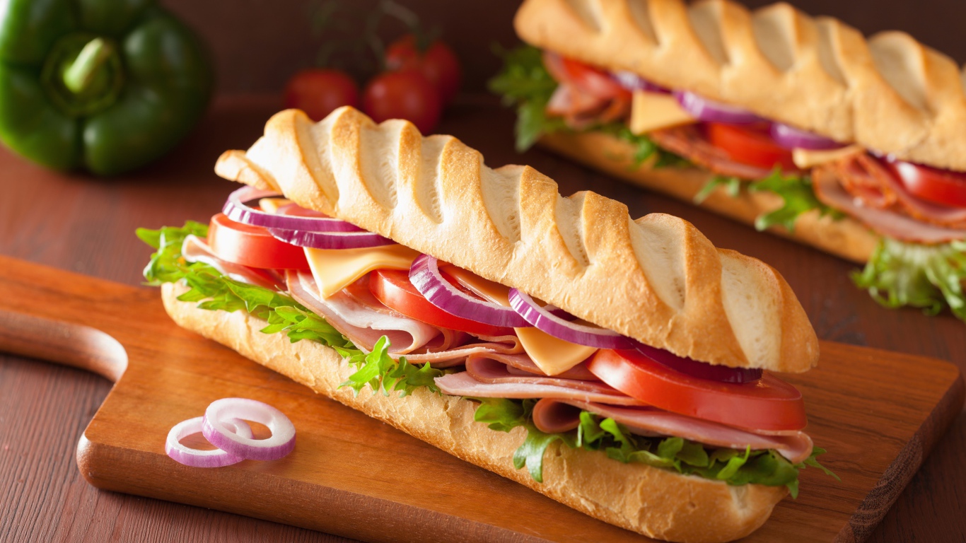 Аппетитный сэндвич с ветчиной, листьями салата, помидорами и луком