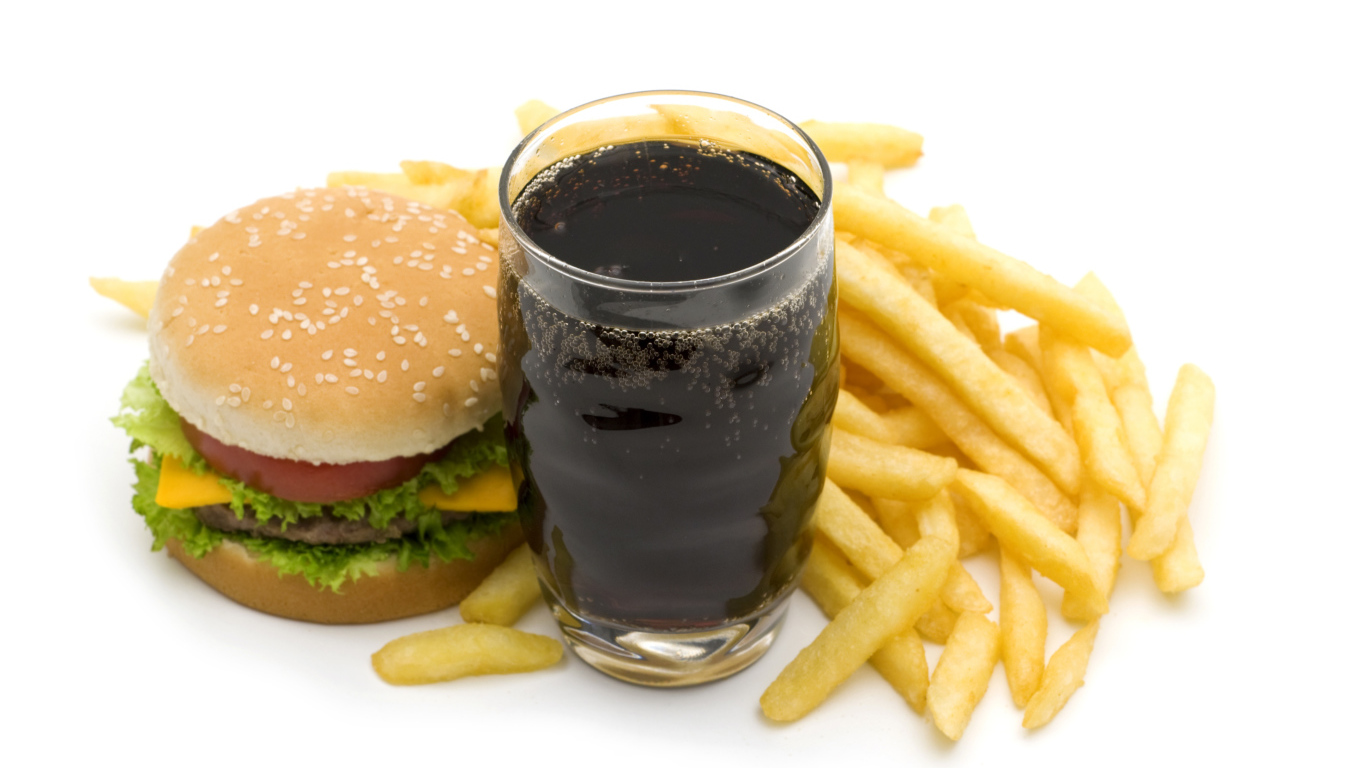 Cola in a glass on a table with a hamburger and french fries on a white background