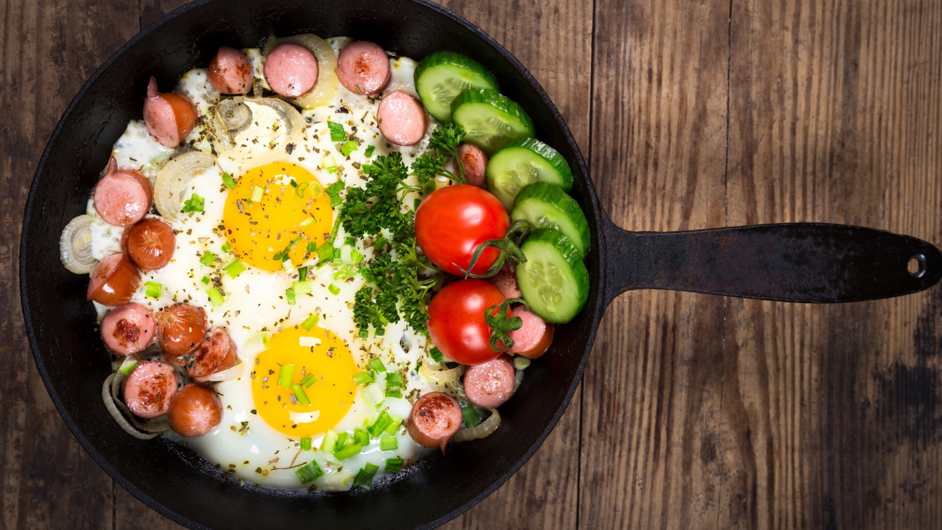 Яичница в сковороде с овощами и кусочками сосиски