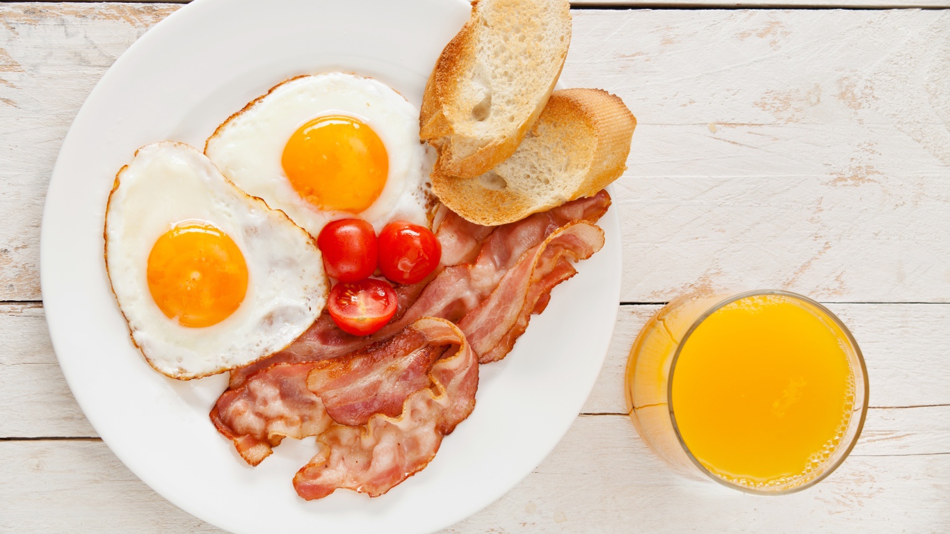 Яичница с беконом, гренками и помидорами на столе с соком 