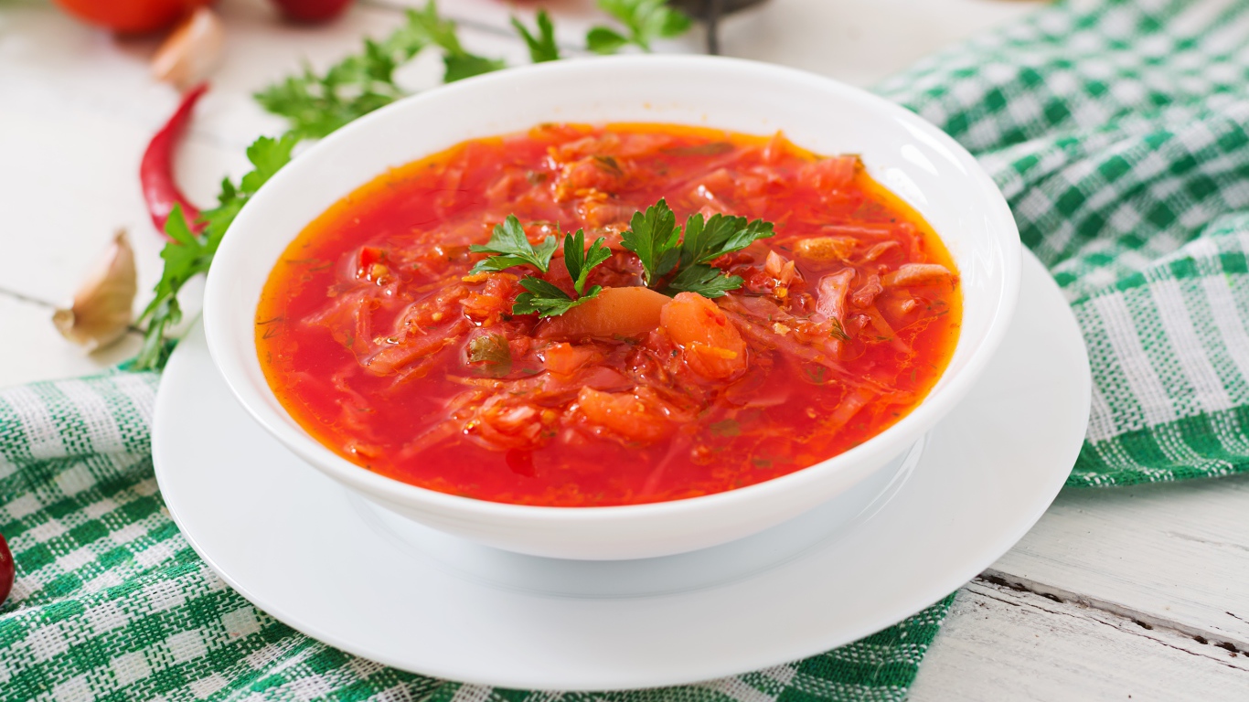 Горячий борщ с зеленью в белой тарелке на столе