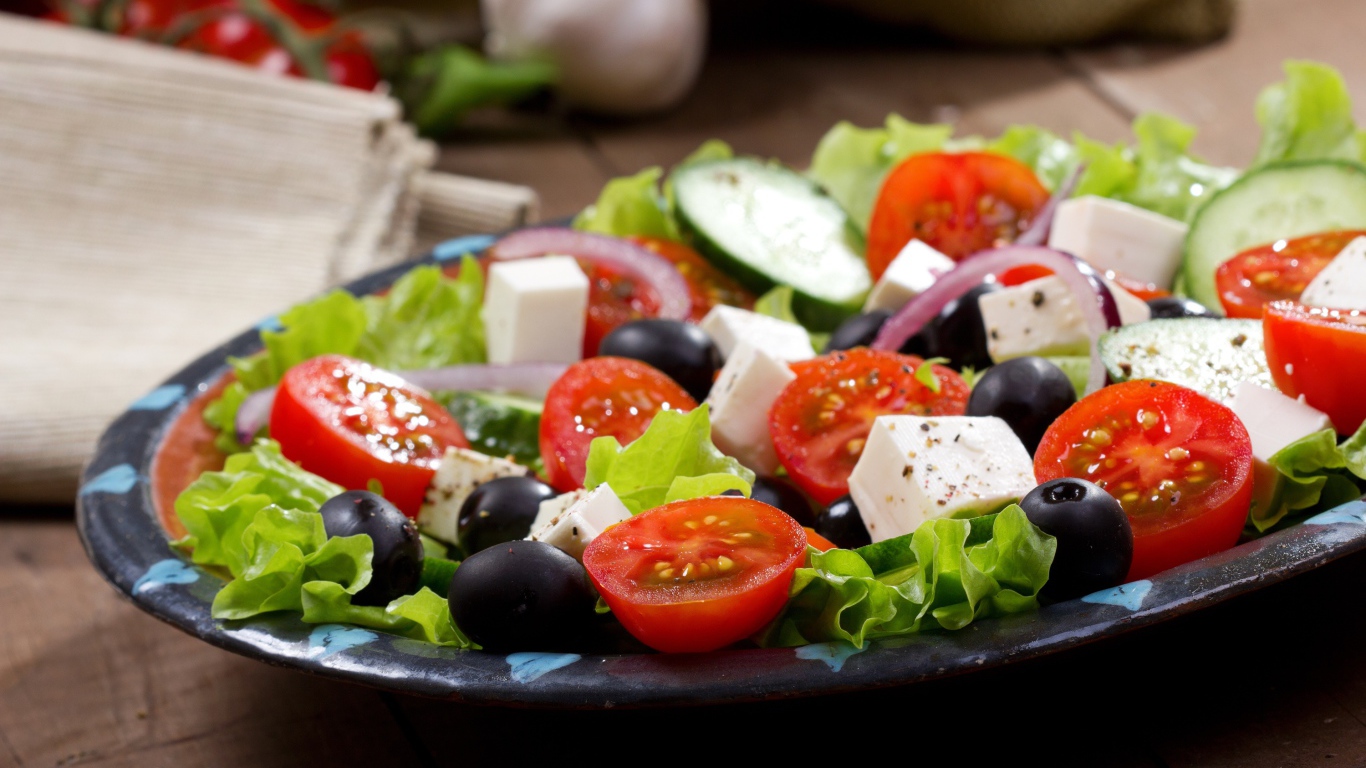 Салат с помидорами, огурцами, оливками, кусочками сыра и луком на листьях салата
