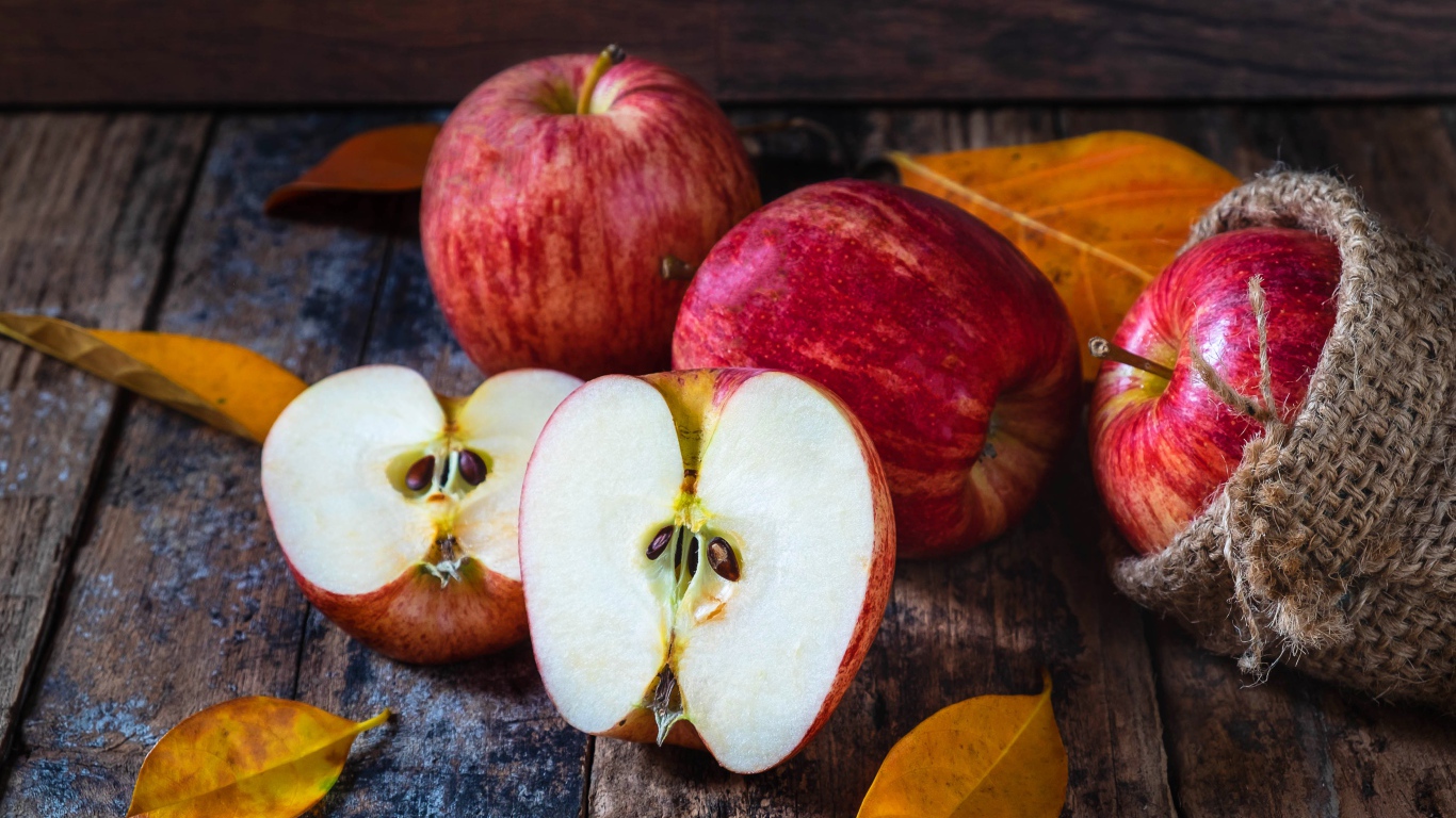 Красивые красные яблоки на столе с желтыми листьями