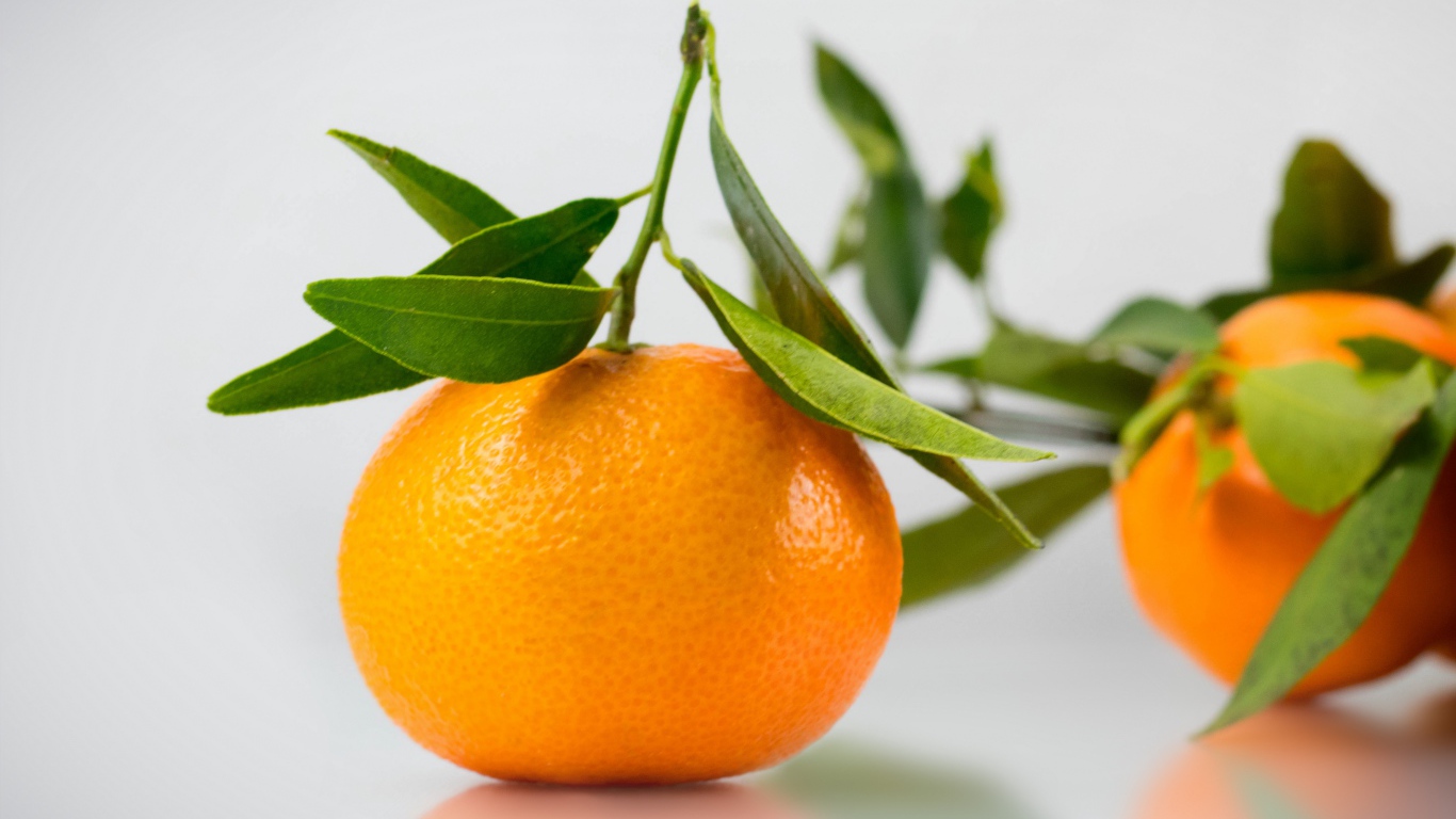 Оранжевый мандарин с зелеными листьями на сером фоне 