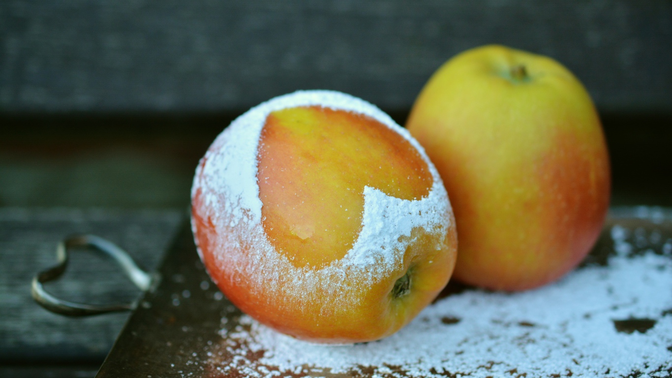 Спелое яблоко с сердцем из сахарной пудры на столе 