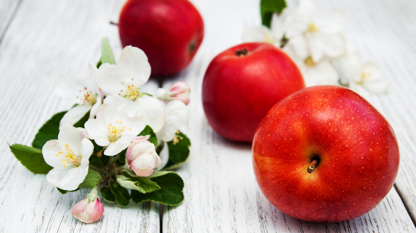 Три красных яблока с цветами на деревянной поверхности