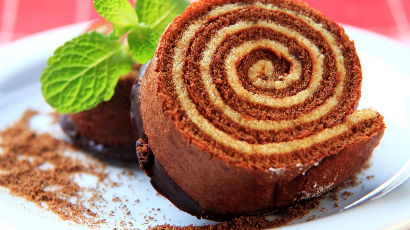 Кусок сладкого рулета с шоколадом и листом мяты на тарелке