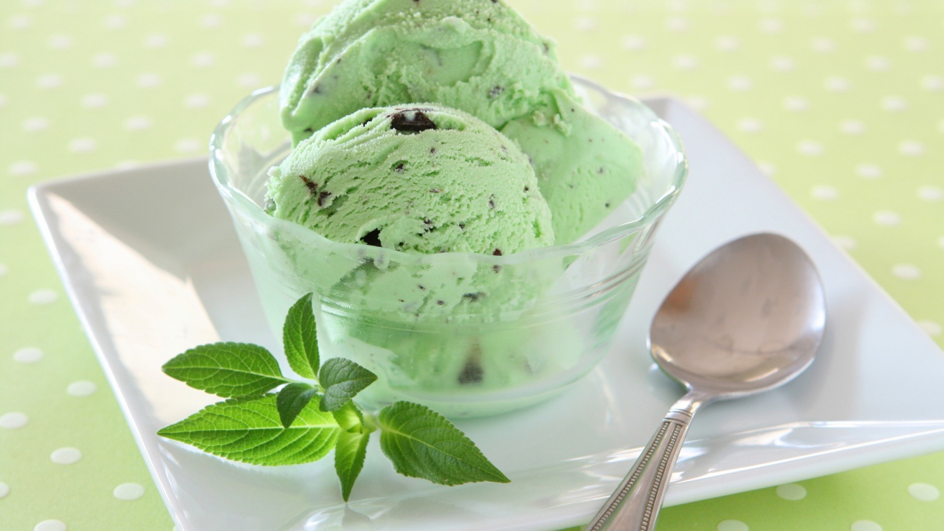 Зеленые шарики мороженого с шоколадом и мятой на тарелке с ложкой