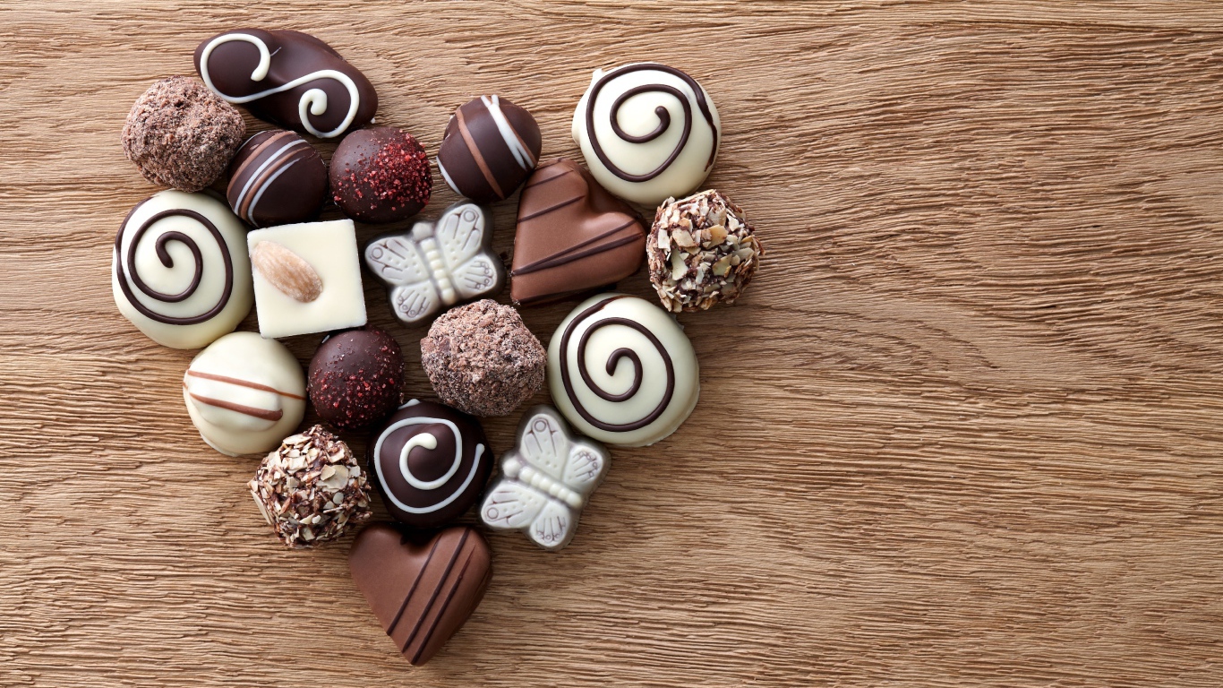 Сердце из шоколадных конфет ассорти на деревянном столе