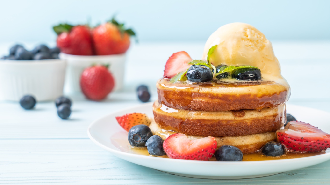 Оладья и медом, мороженым и ягодами черники и клубники на столе