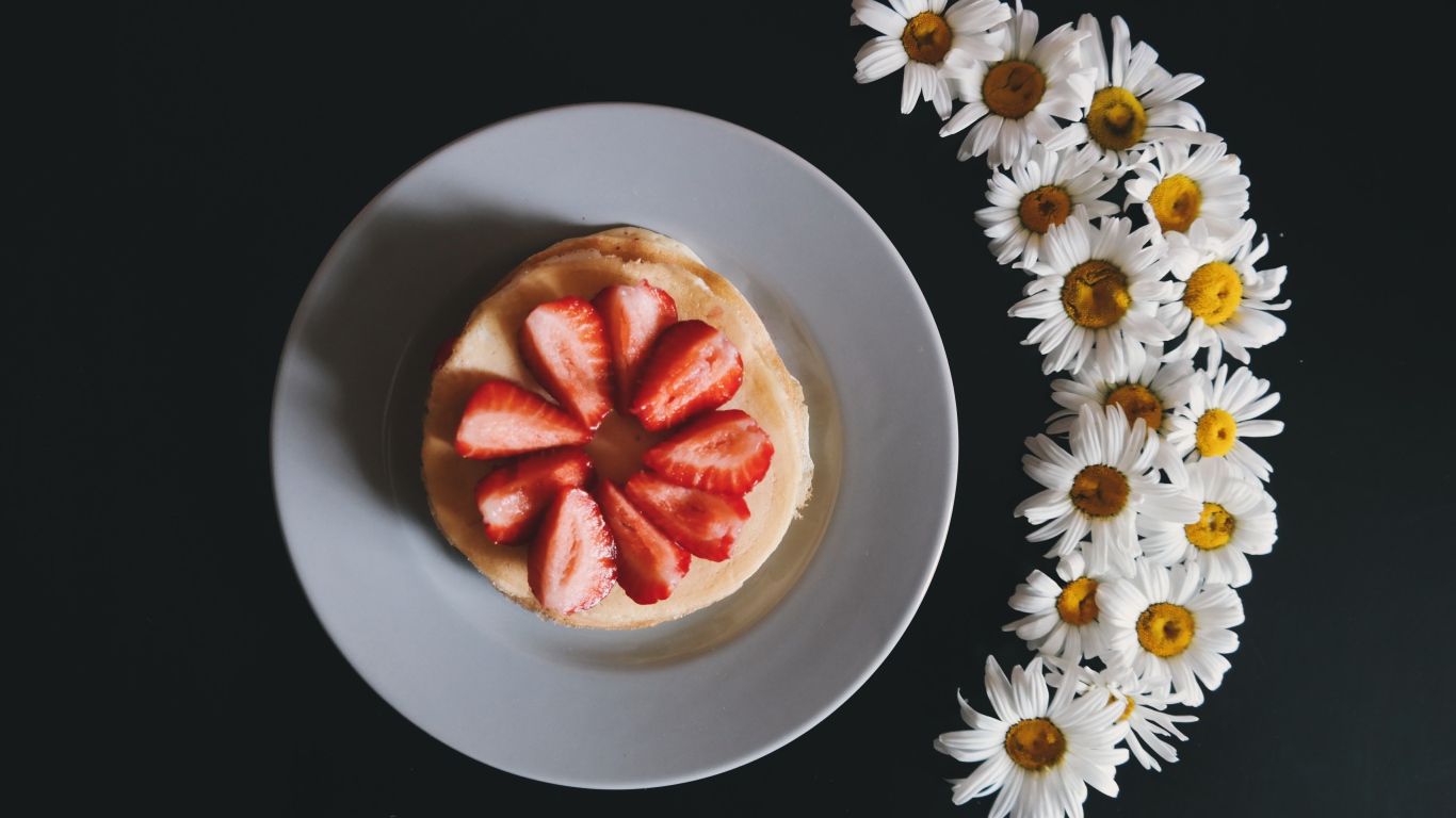 Оладьи с клубникой на тарелке на сером фоне с ромашками