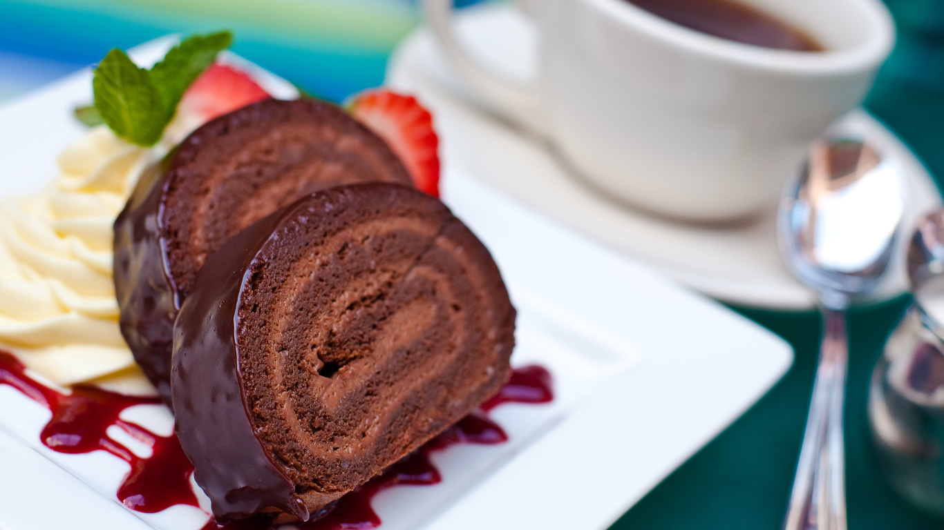 Сладкий рулет с клубничным джемом и чашкой чая на столе