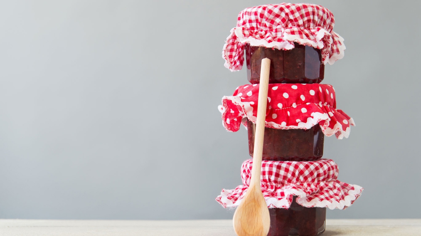 Три баночки варенья с деревянной ложкой на сером фоне