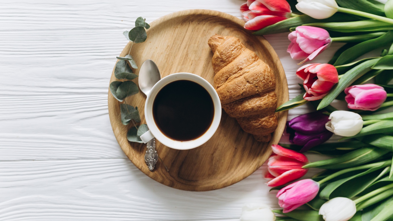 Чашка кофе с круассаном на столе с букетом тюльпанов 