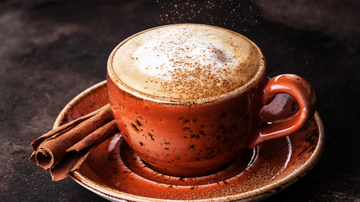 Чашка кофе с пенкой на блюдце с корицей