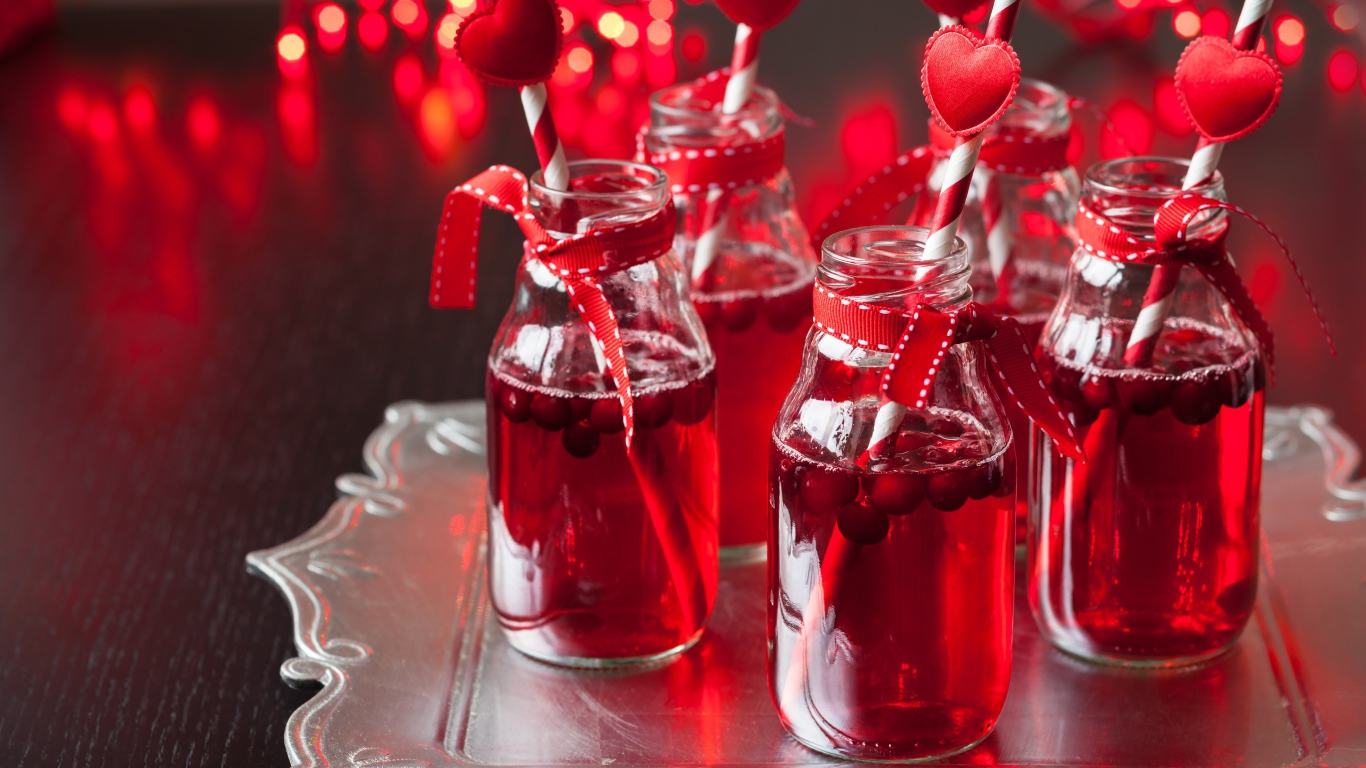 Вкусный напиток с клюквой в стеклянных бутылках на столе с трубочками