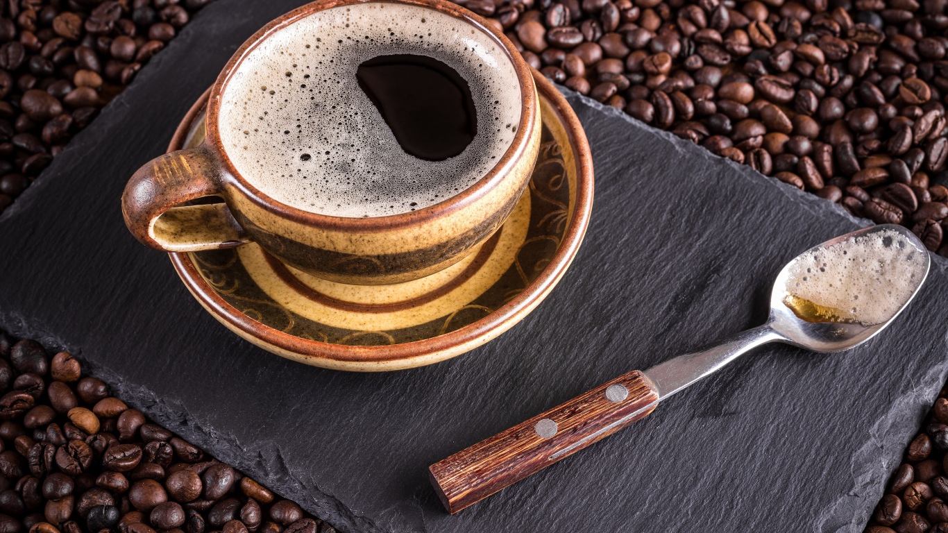 Большая чашка кофе с чайной ложкой стоят на кофейных зернах